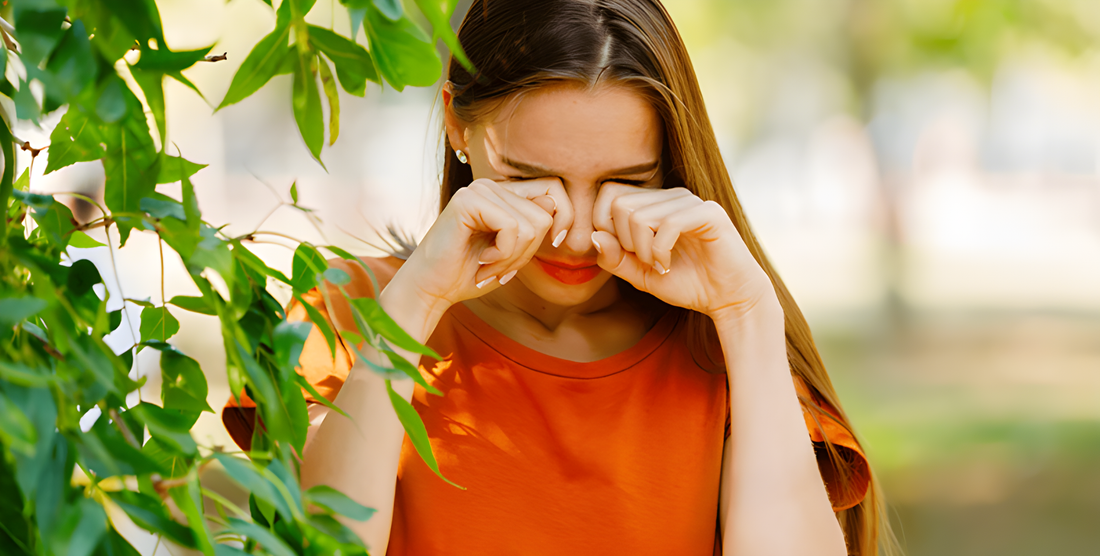 Ragazza all'aperto tra il verde si strofina gli occhi arrossati per il prurito da allergia primaverile