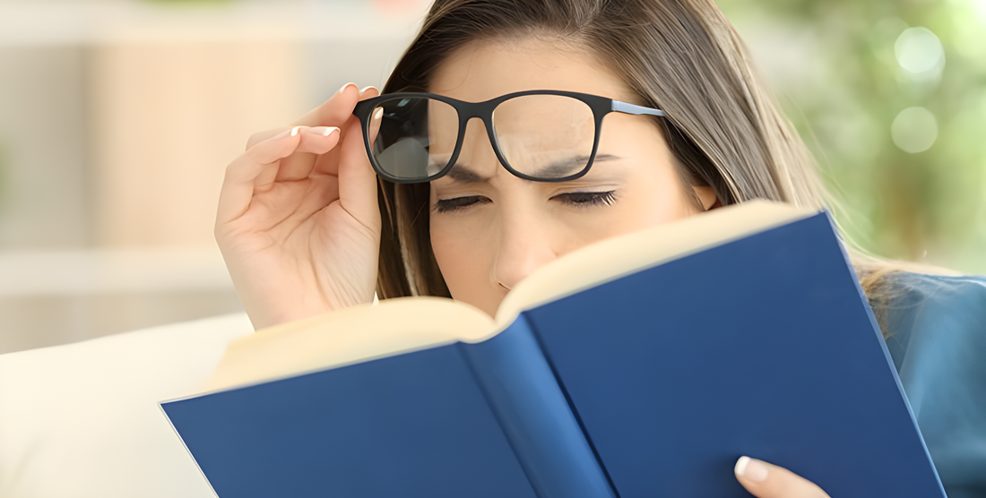 Donna solleva gli occhiali e socchiude gli occhi cercando di leggere un libro, difficoltà di messa a fuoco