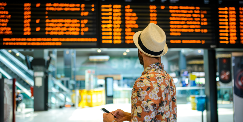 Uomo socchiude gli occhi per leggere il tabellone orari in stazione, come vede chi ha l'astigmatismo