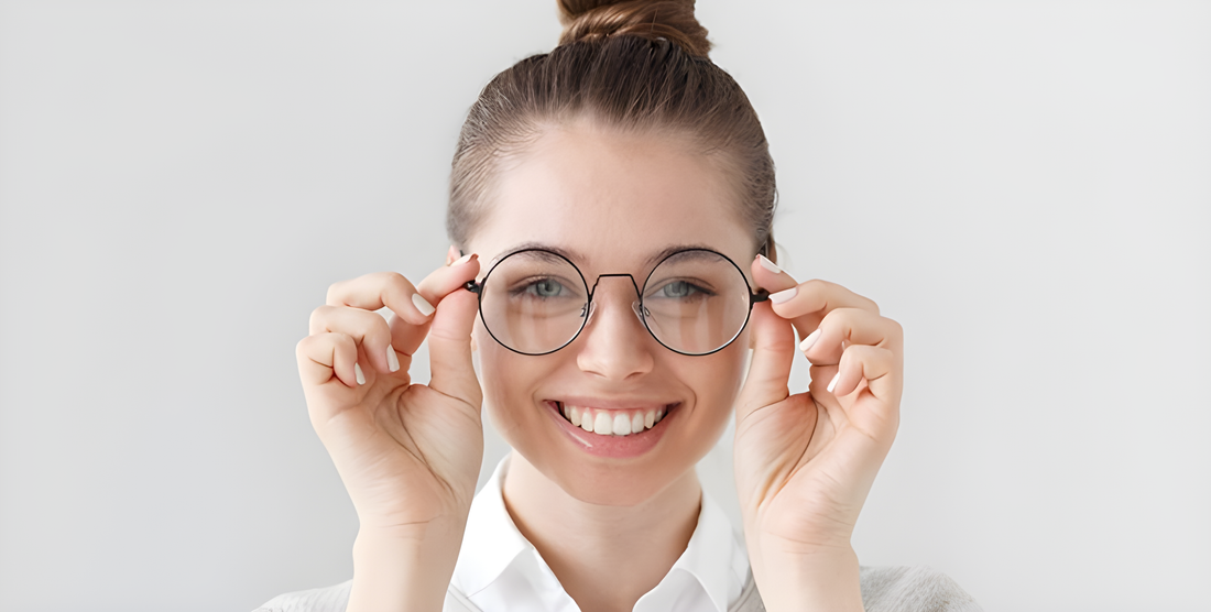 Donna sorridente tiene con entrambe le mani gli occhiali tondi dallo stile nerd-chic