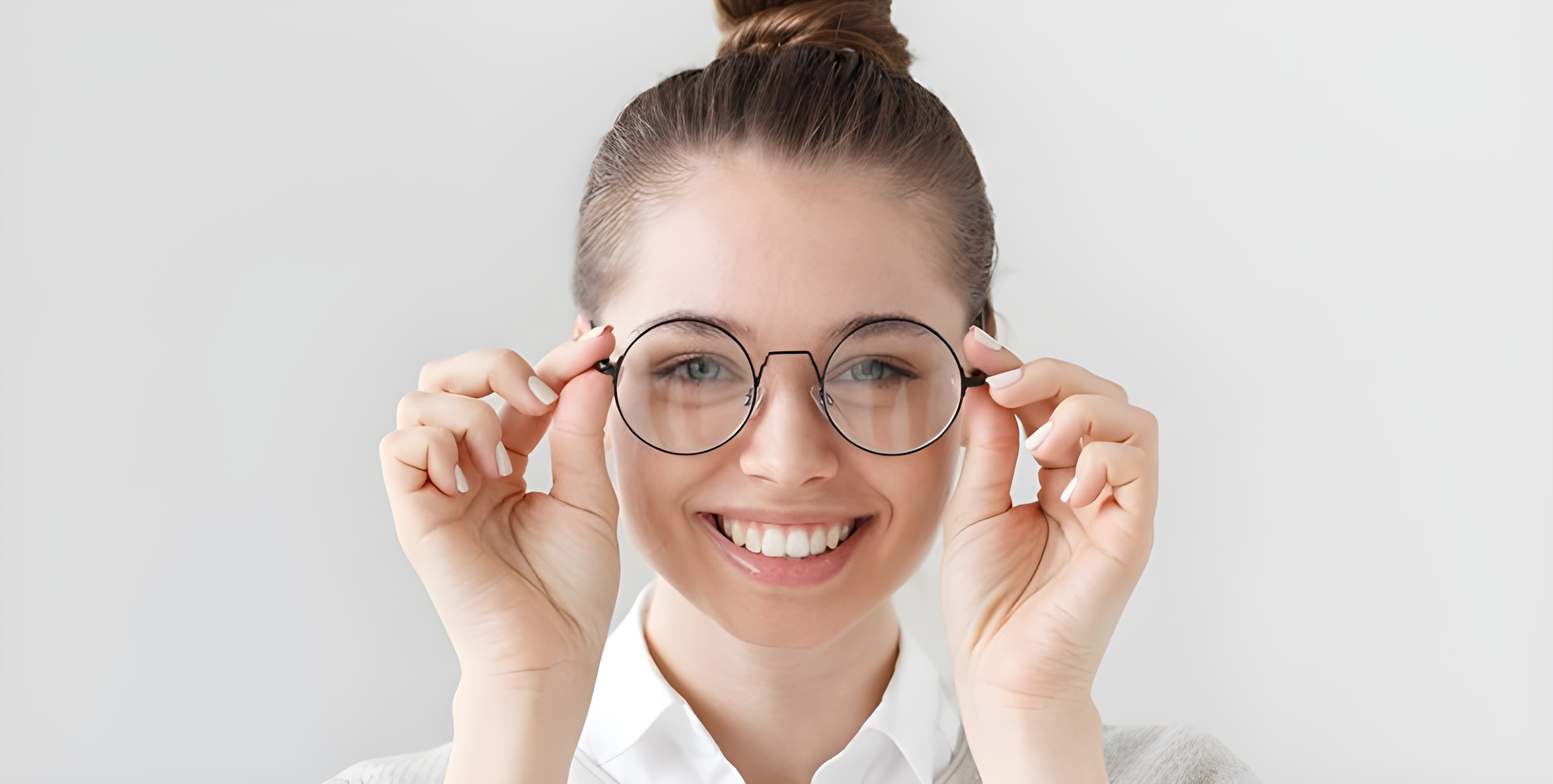 Donna sorridente tiene con entrambe le mani gli occhiali tondi dallo stile nerd-chic