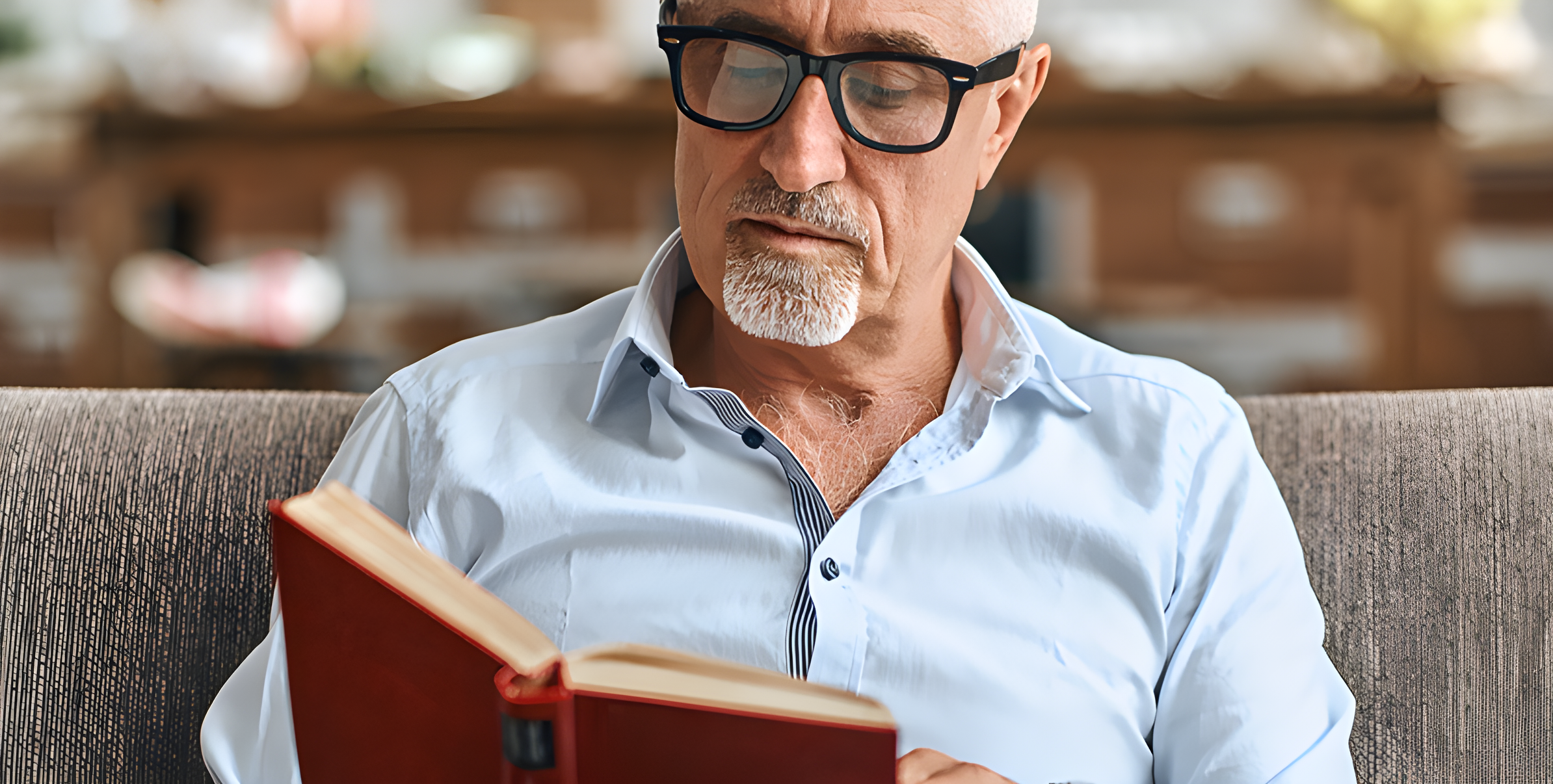 Uomo maturo legge un libro con gli occhiali seduto sul divano