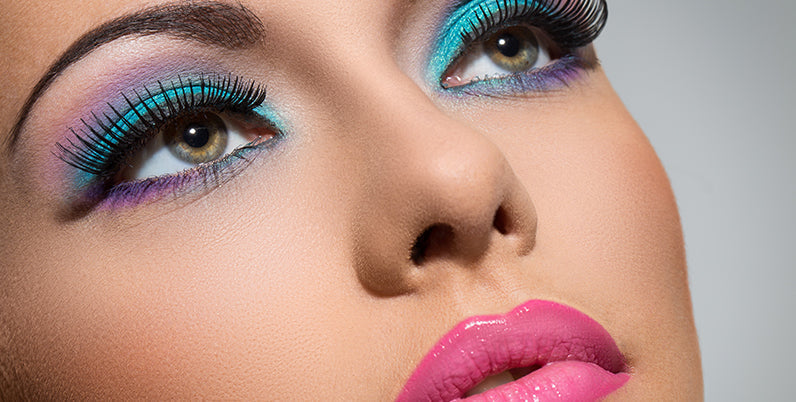 Primo piano di volto femminile con trucco occhi azzurro e viola e labbra rosa, look primavera-estate