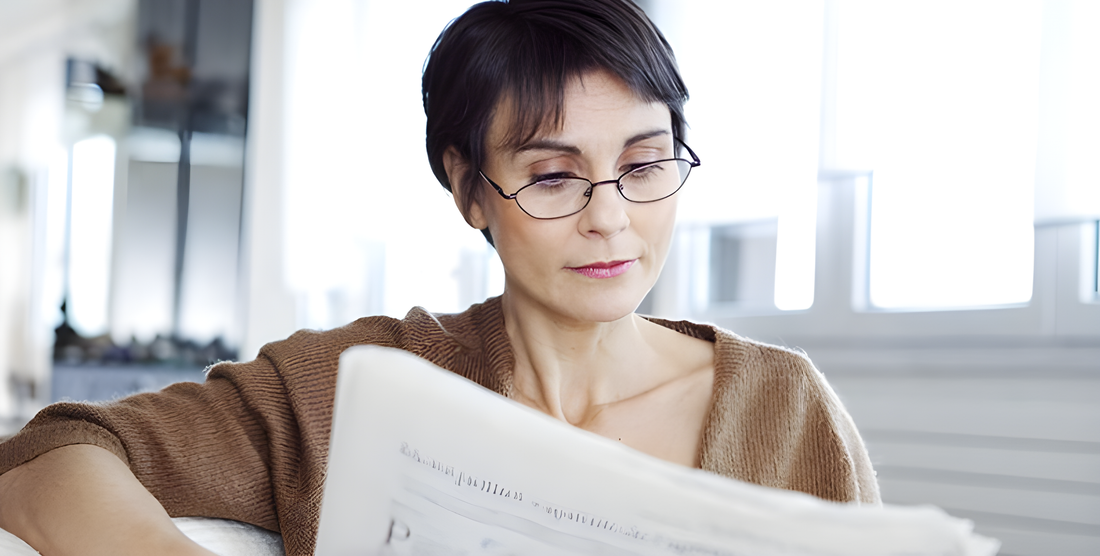 Donna matura legge il giornale con gli occhiali da lettura abbassati sul naso