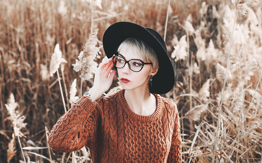 Donna con cappello e occhiali da vista in un campo di canne, look autunnale