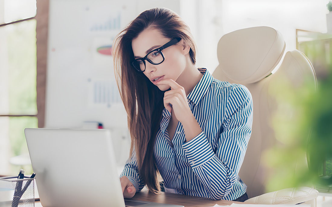 Donna con occhiali da vista pensierosa davanti al portatile sul posto di lavoro