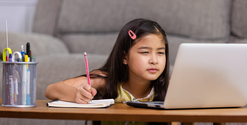 Bambina studia scrivendo su un quaderno davanti al portatile, tema della progressione miopica