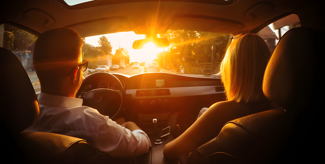 Coppia in auto verso il sole al tramonto: le lenti polarizzate riducono l'abbagliamento alla guida
