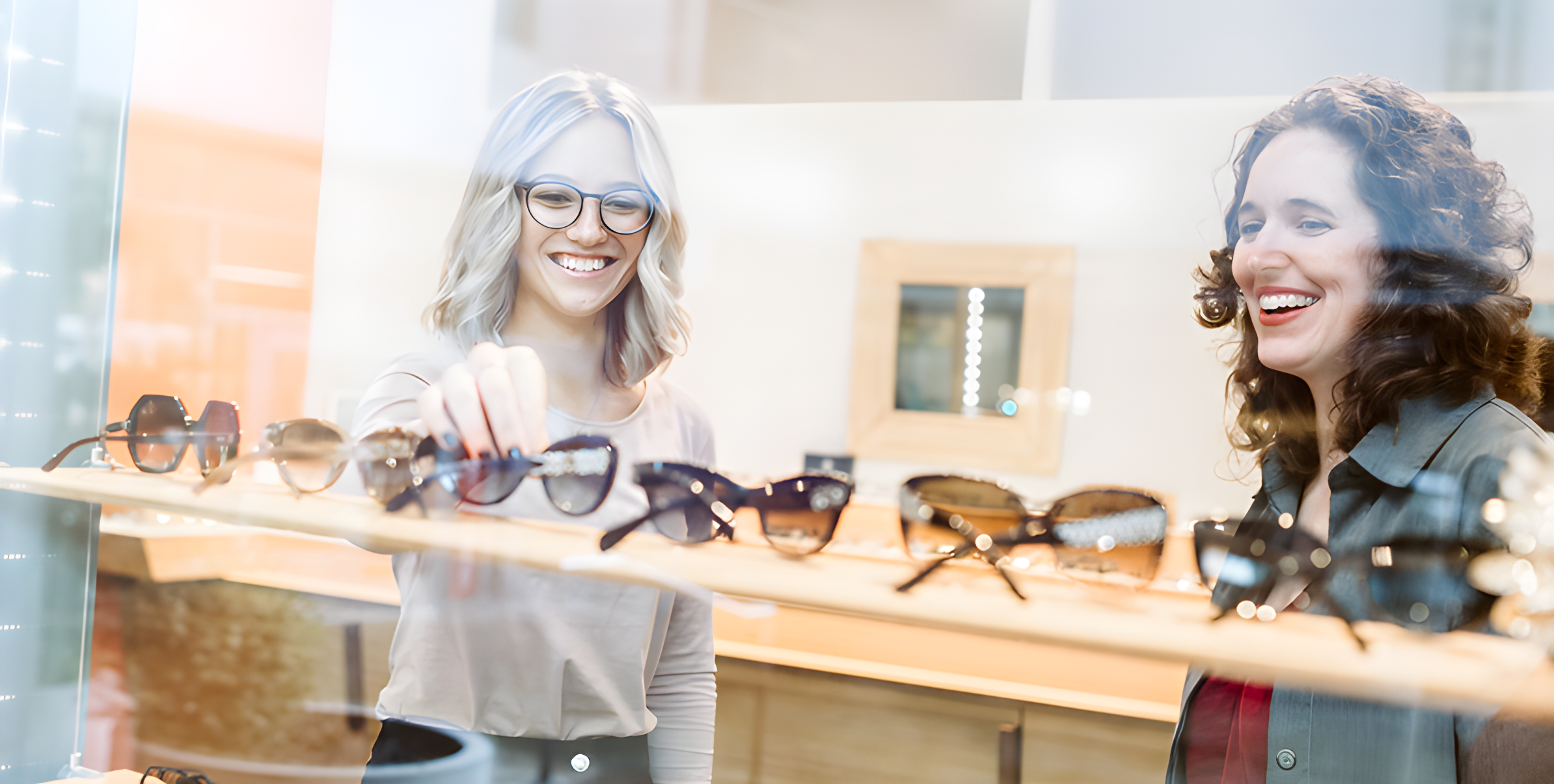 Due donne sorridenti guardano gli occhiali da sole esposti nella vetrina di un negozio