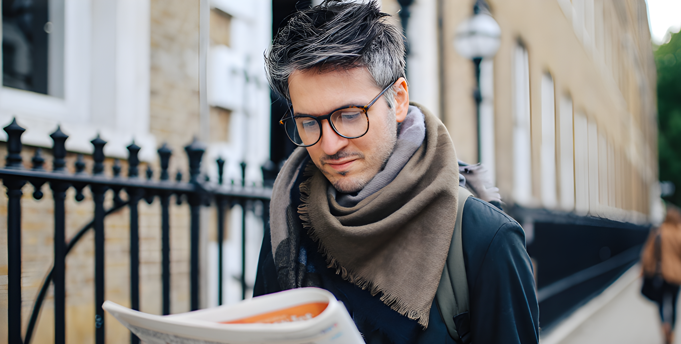 Uomo dai capelli brizzolati con occhiali e sciarpa legge il giornale per strada, stile vintage