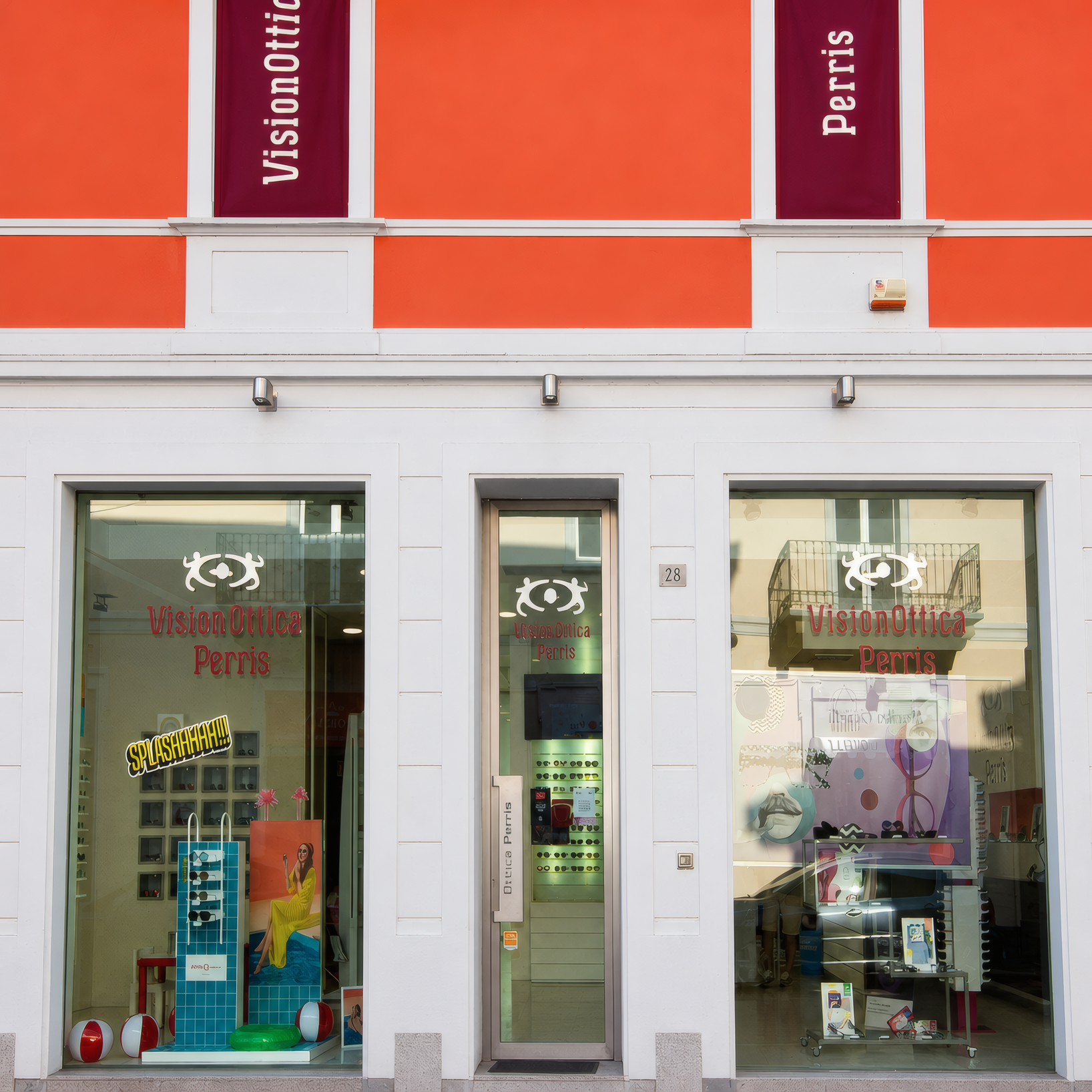 Facciata del negozio VisionOttica Perris di Rho su edificio con facciata arancione e tre vetrine affiancate, insegne verticali con nome, porta chiusa con cartello 'Chiuso' e vetrina con abbigliamento esposto