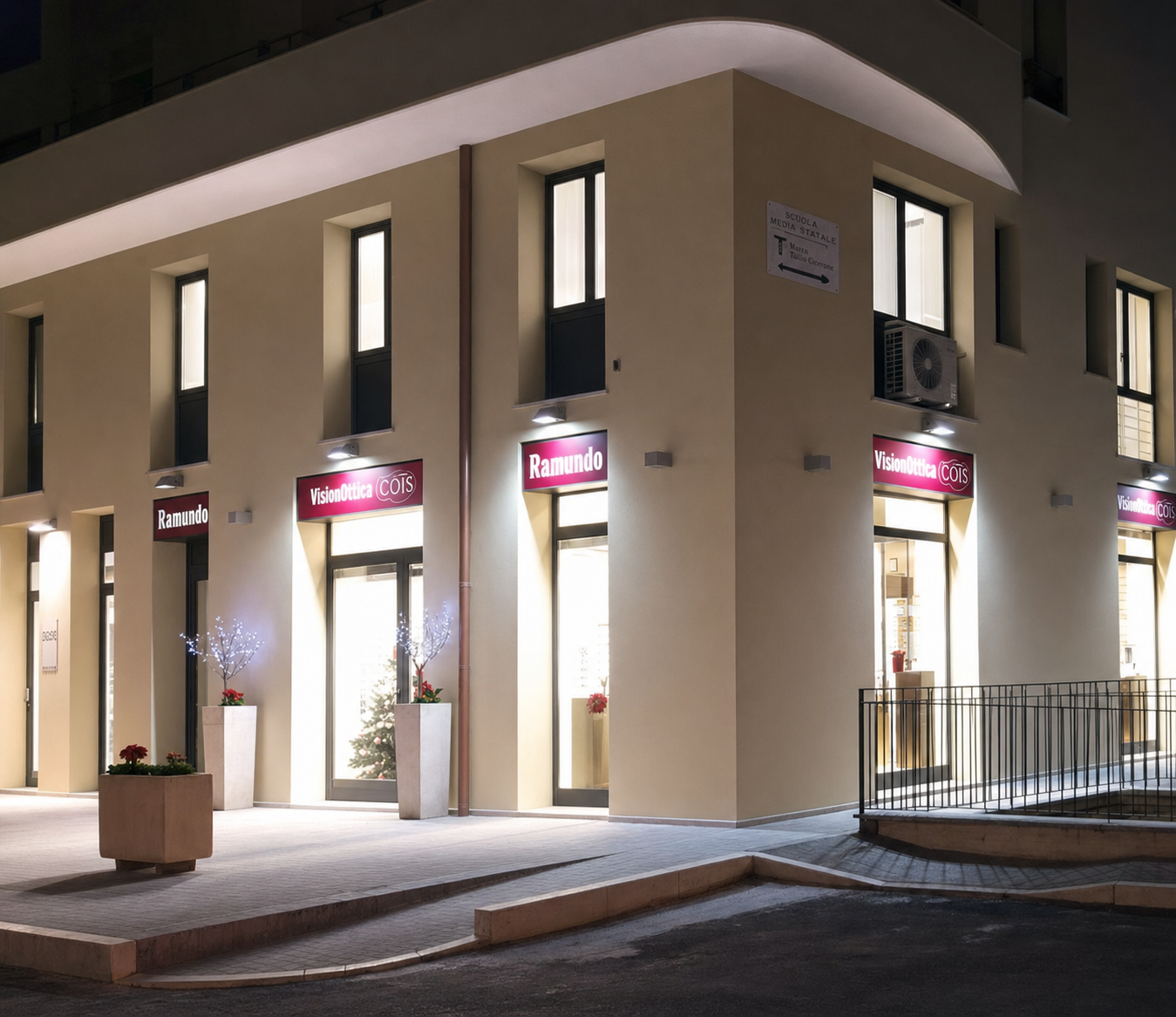 Facciata del negozio VisionOttica Ramundo di Nardò su angolo strada fotografata di notte con insegne bordeaux luminose su due lati e finestre illuminate dell'interno