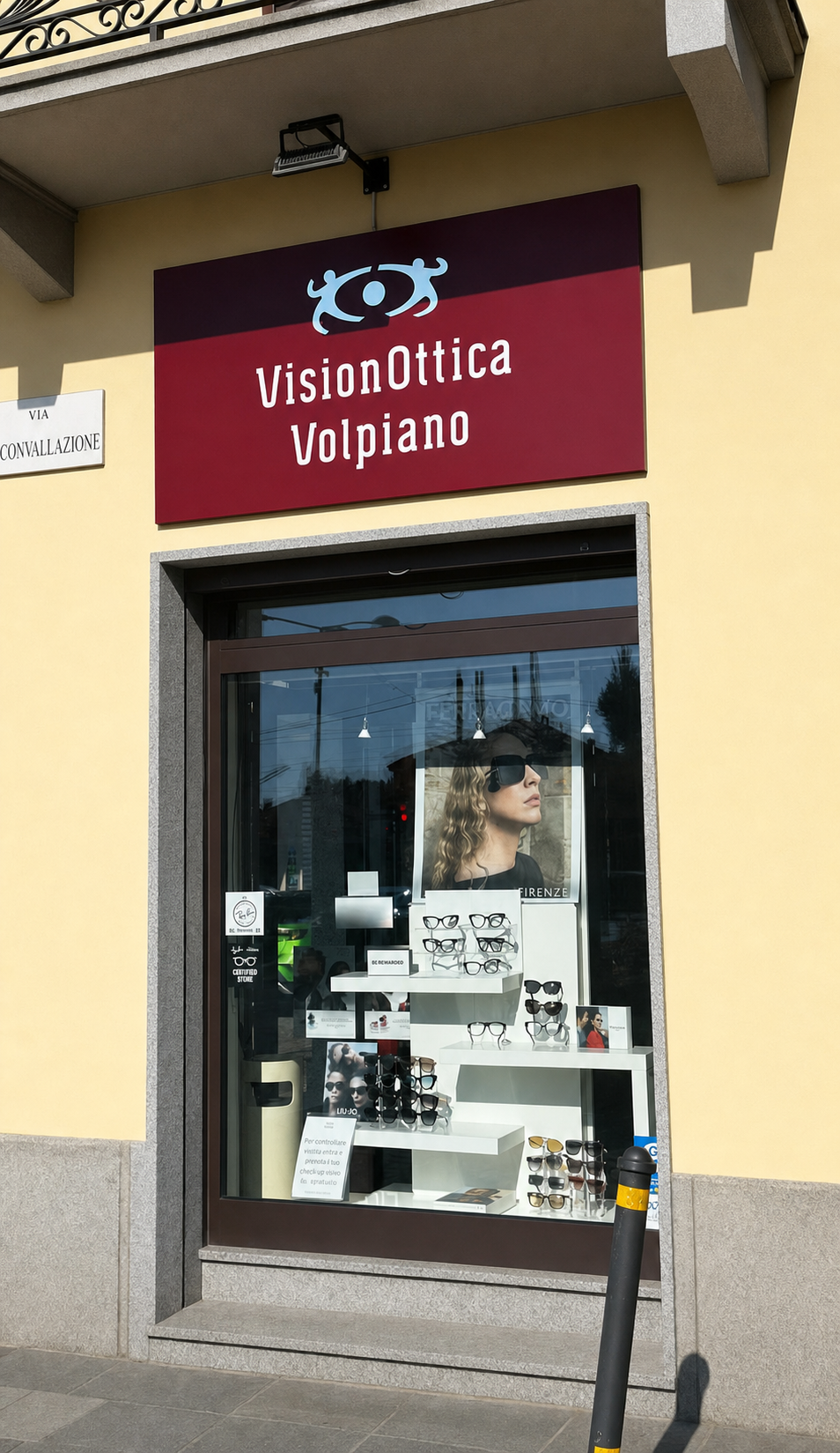 Vetrina del negozio VisionOttica Volpiano di Volpiano su strada con insegna bordeaux, allestimento con manichino in occhiali da sole e piccoli espositori con montature sul davanzale