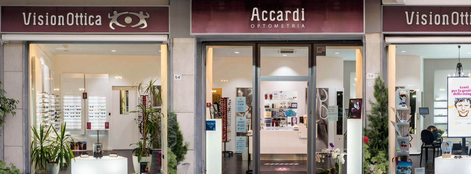 Facciata del negozio VisionOttica Accardi di Palermo in centro commerciale con tre moduli affiancati, insegne bordeaux, porta centrale a vetri e vetrine laterali con espositori di montature e piante decorative