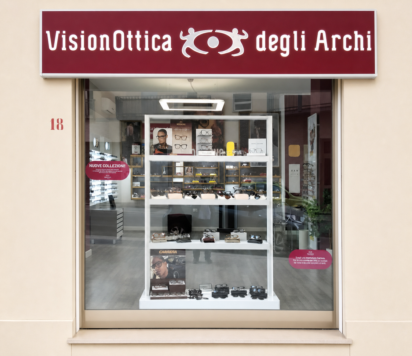 Vetrina del negozio VisionOttica degli Archi di Trapani su strada con espositore a ripiani bianchi, montature da vista e da sole e insegna bordeaux con logo