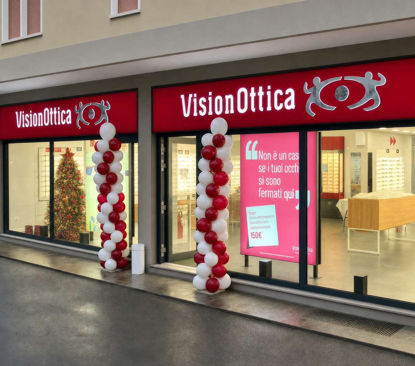 Facciata del negozio VisionOttica Belluno su strada con insegna rossa, colonne di palloncini rossi e bianchi, vetrina con albero di Natale e banner promozionale