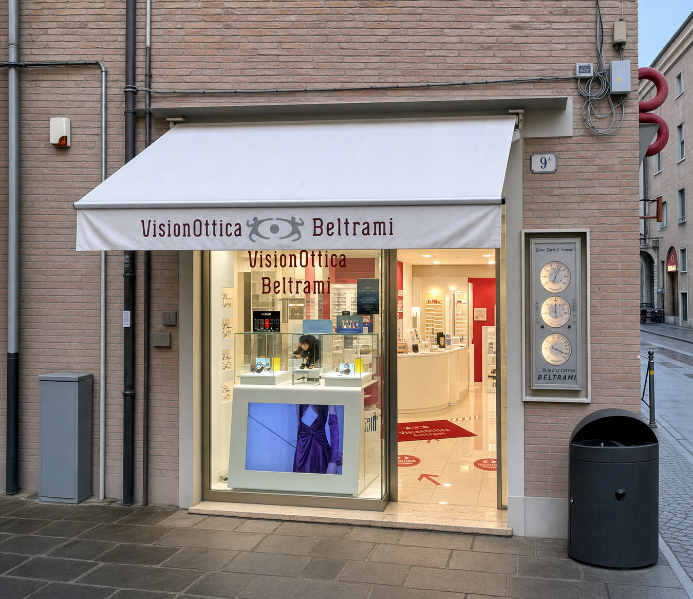 Vetrina del negozio VisionOttica Beltrami di Ferrara in centro storico su angolo con tenda bianca, espositori illuminati con occhiali e insegna sul tendone