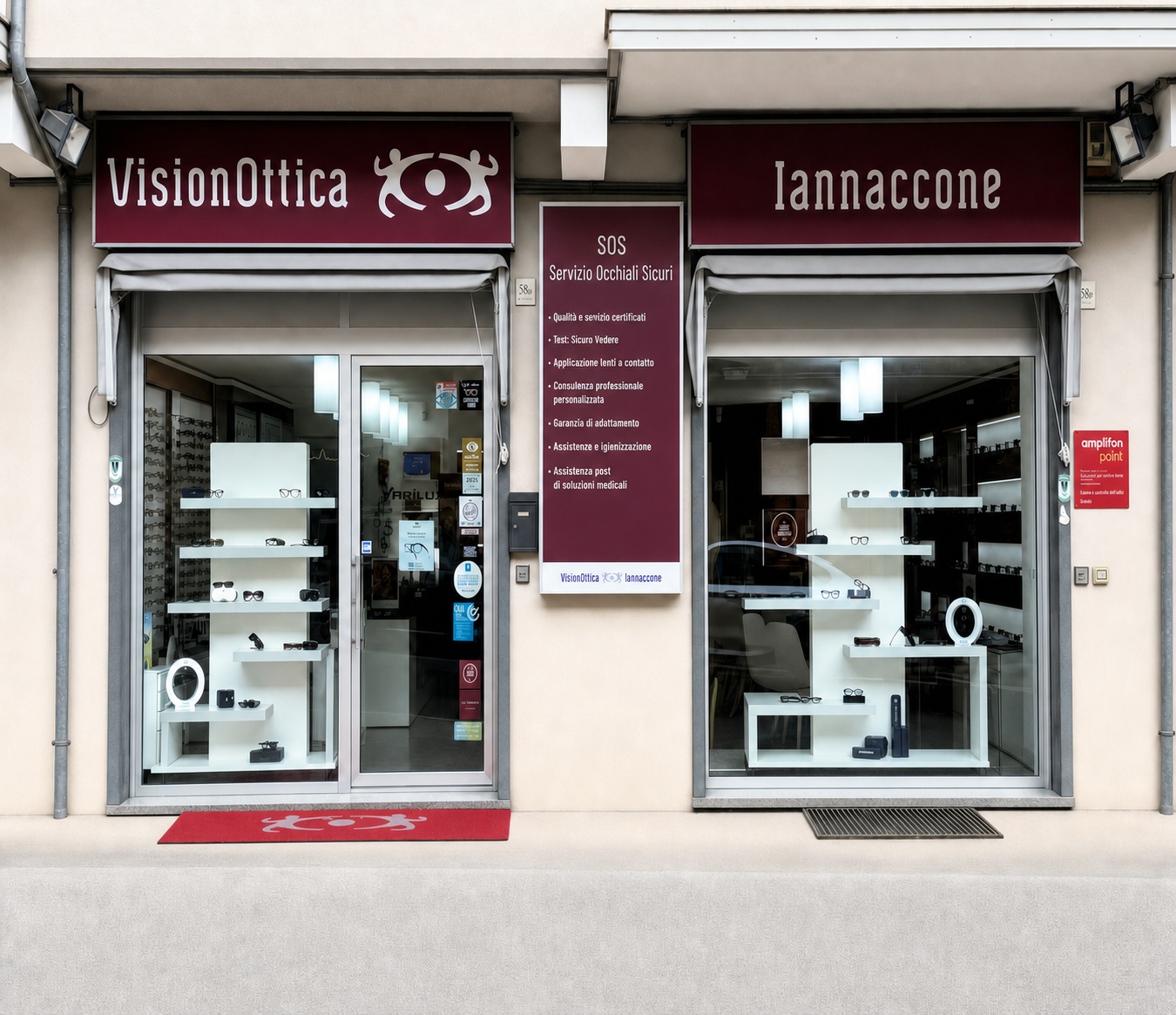 Facciata del negozio VisionOttica Iannaccone di Montella su strada con doppia vetrina, insegna bordeaux, tappeto rosso all'ingresso e pannello SOS Servizi Occhiali Sicuri