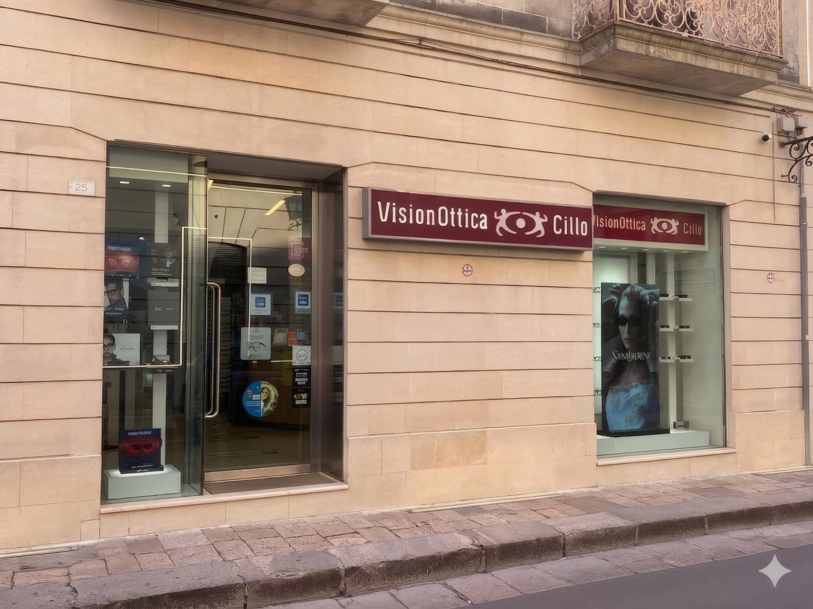 Facciata del negozio VisionOttica Cillo di Maglie in centro storico su strada con insegna bordeaux doppia, vetrina con poster Saint Laurent e porta scorrevole a vetri