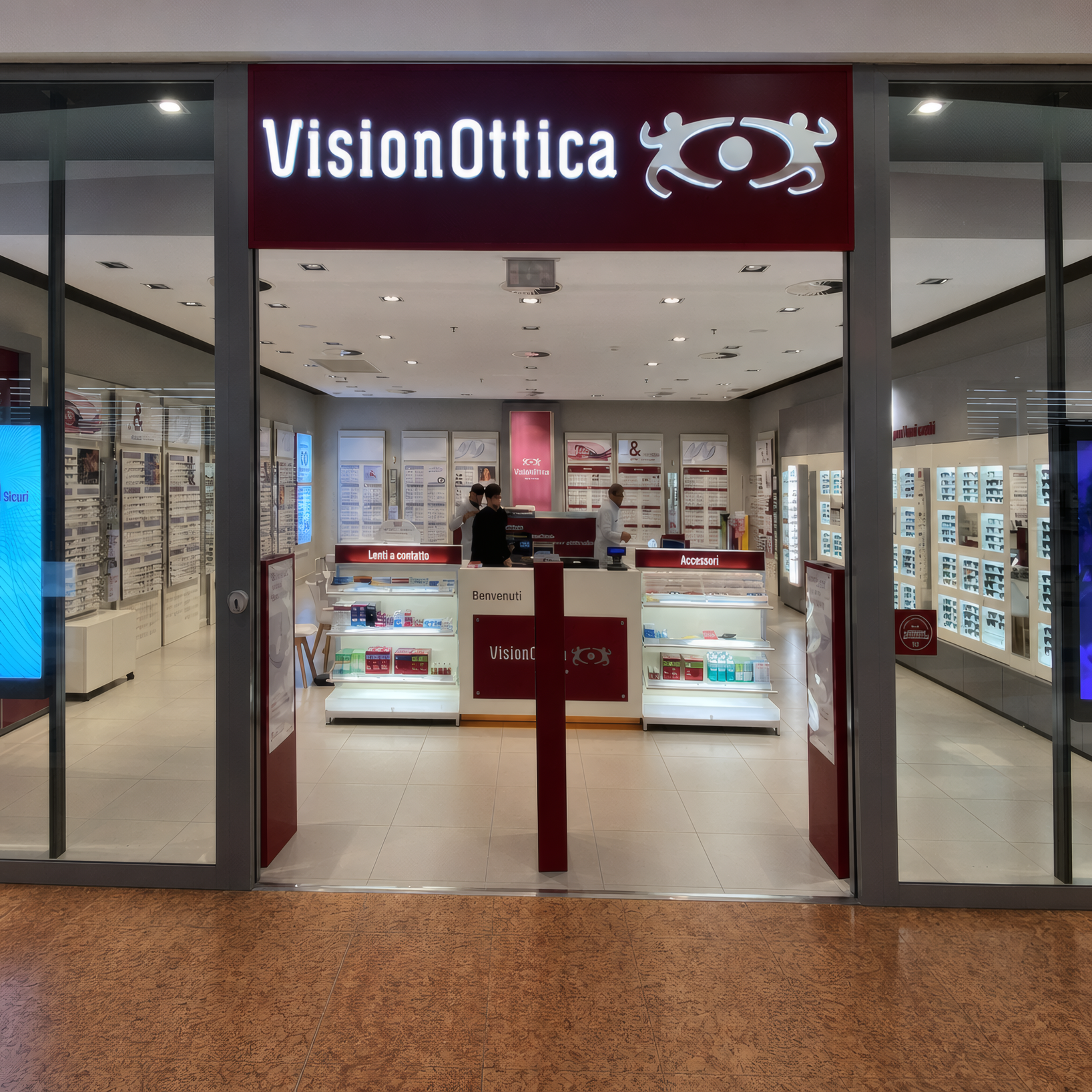 Ingresso del negozio VisionOttica Val Vibrata di Colonnella in centro commerciale con insegna bordeaux illuminata, porta a vetri e interno con espositori di montature e bancone centrale