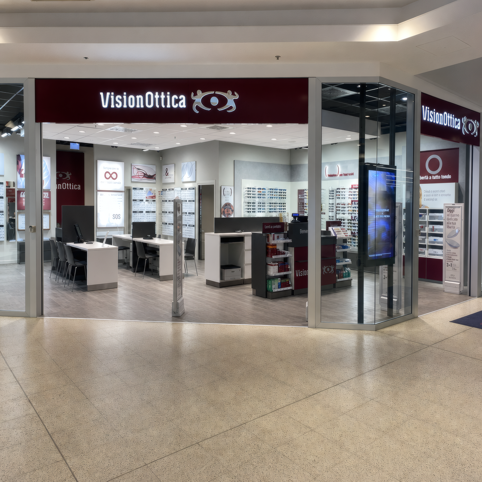 Ingresso del negozio VisionOttica Treviglio di Treviglio in centro commerciale con doppia insegna bordeaux, interno aperto con bancone bianco, espositori e totem digitali