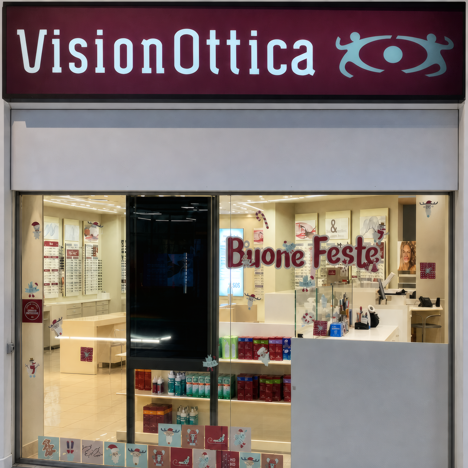 Ingresso del negozio VisionOttica Virgilio di Cerese in centro commerciale con insegna bordeaux, vetrina con banner stagionale Buone Feste e interno con espositori di prodotti ottici