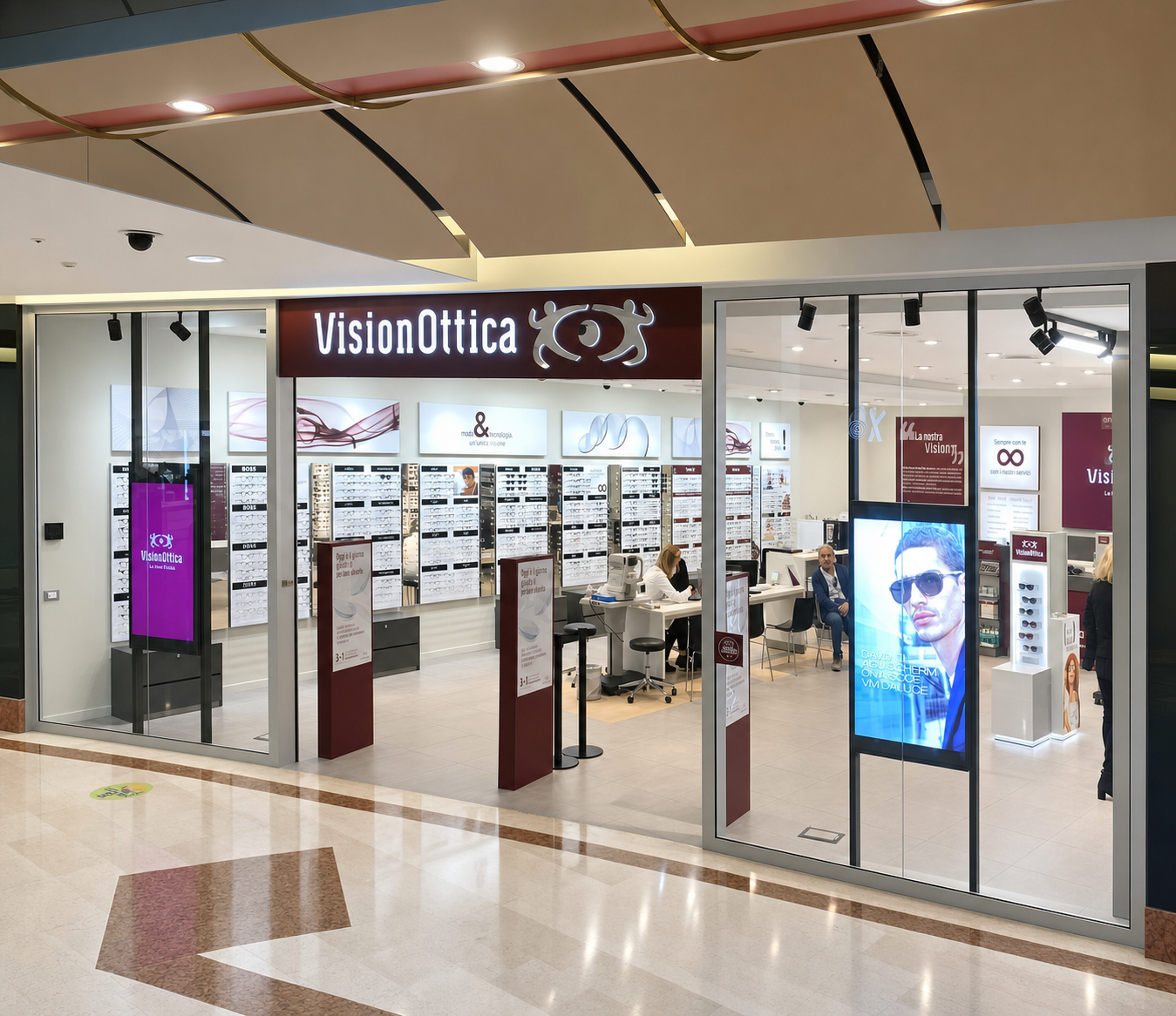 Ingresso del negozio VisionOttica Porte di Mestre di Mestre in centro commerciale con insegna bordeaux, ampia apertura, espositori di occhiali a parete e totem digitale con immagine di uomo con occhiali da sole