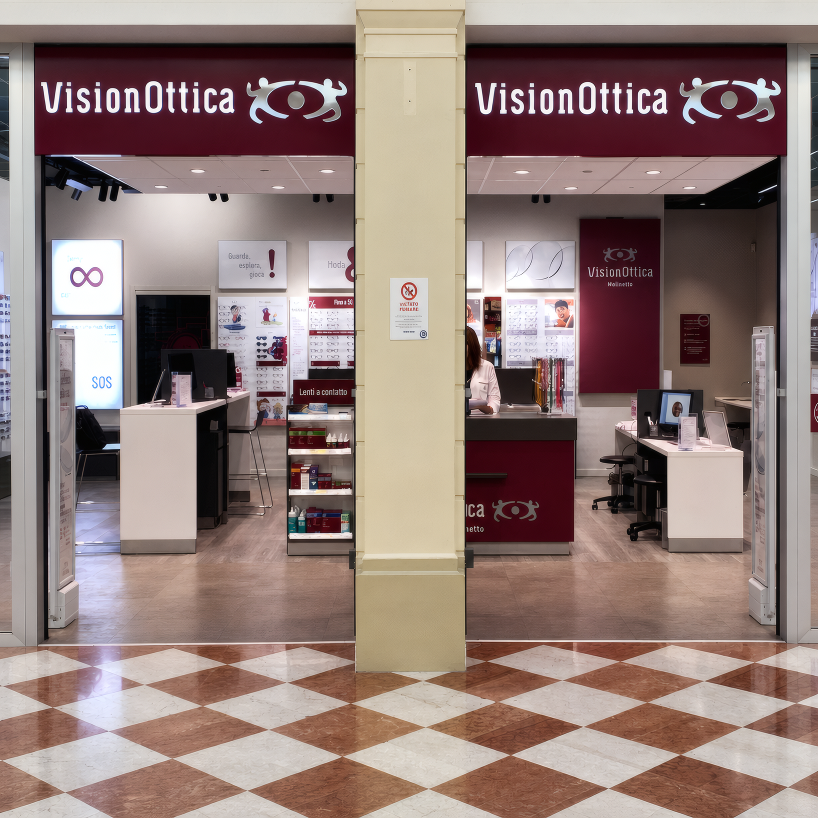 Ingresso del negozio VisionOttica Molinetto di Mazzano in centro commerciale con doppia insegna bordeaux su pilastro centrale, doppio accesso a vetri e interno con espositori bianchi e bancone
