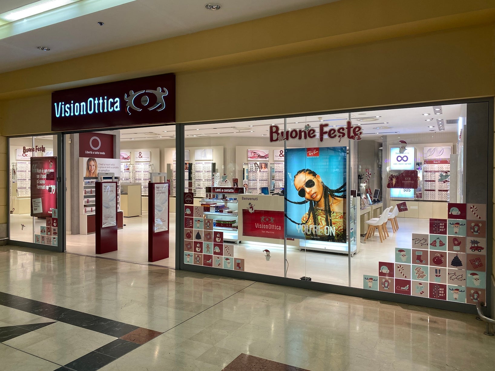 Vetrina del negozio VisionOttica San Martino di San Martino Siccomario in centro commerciale con decorazioni natalizie Buone Feste, campagna Ray-Ban e insegna nera con logo