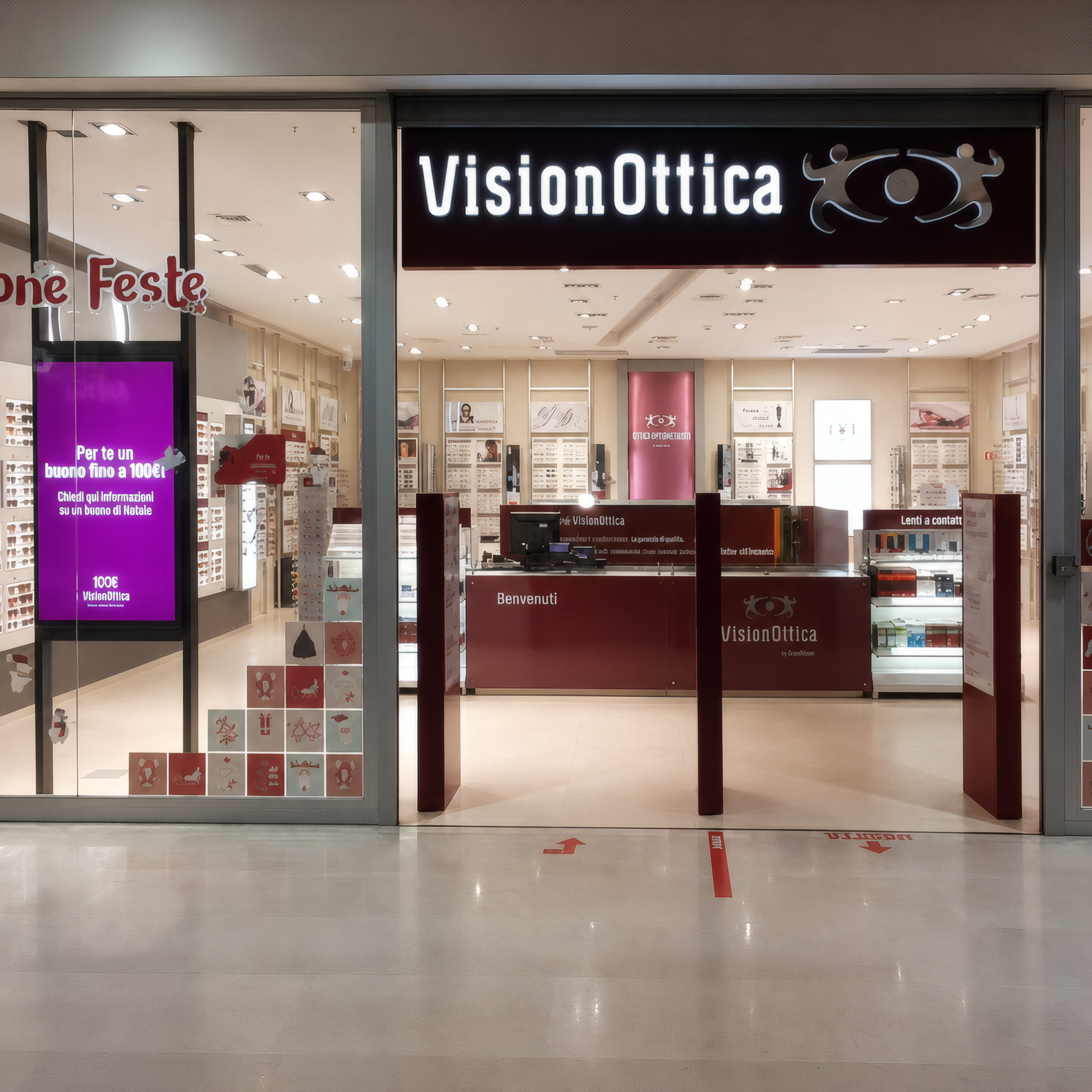 Ingresso del negozio VisionOttica Il Ducale di Vigevano in centro commerciale con insegna bordeaux su fascia scura, vetrine con decorazioni natalizie e bancone centrale visibile
