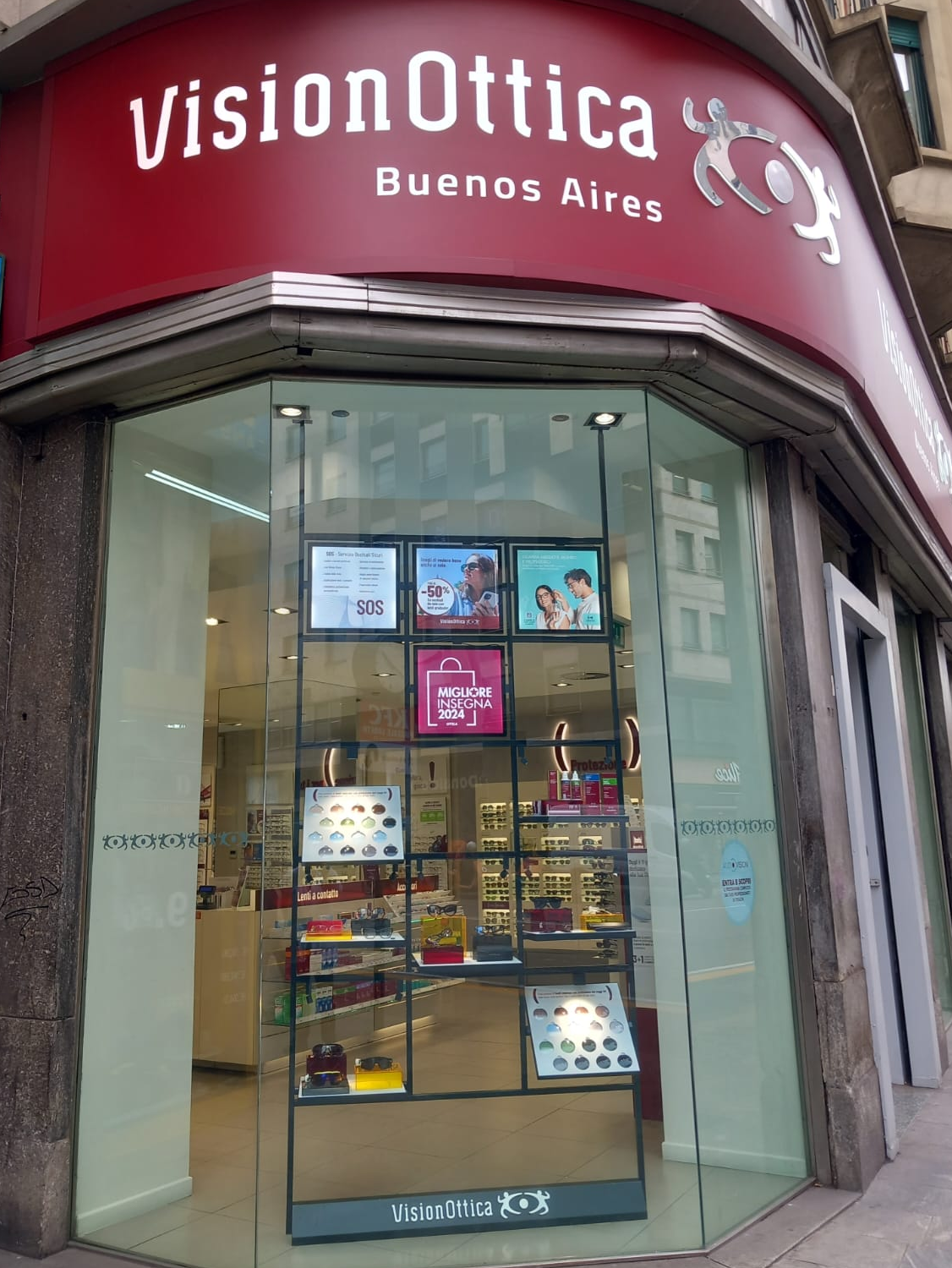 Vetrina angolare del negozio VisionOttica Buenos Aires di Milano su via Buenos Aires con insegna rossa, vetrinetta con espositori di occhiali e badge Migliore Insegna 2024