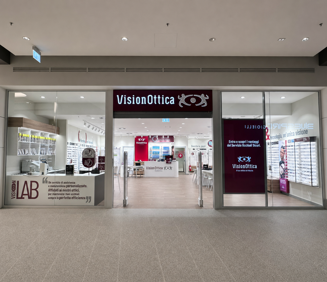 Ingresso del negozio VisionOttica Waterfront di Genova in centro commerciale con insegna bordeaux su fondo bianco, totem Lab laterale e schermo digitale promozionale