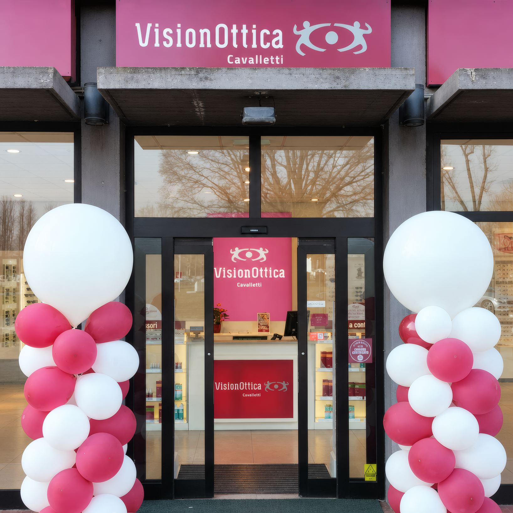 Facciata del negozio VisionOttica Le Mura di Lucca su strada con insegna bordeaux Cavalletti, porta a vetri centrale e decorazioni a palloncini rosa e bianchi per inaugurazione