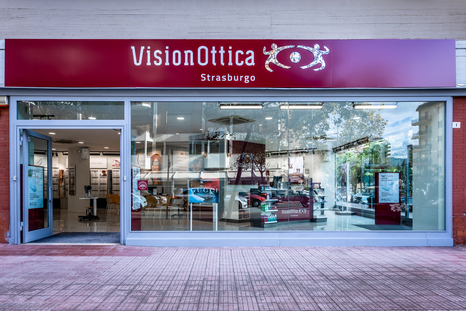 Vetrina del negozio VisionOttica Strasburgo di Palermo su strada con ampia vetrata panoramica, insegna bordeaux con sottotitolo Strasburgo e espositori interni visibili