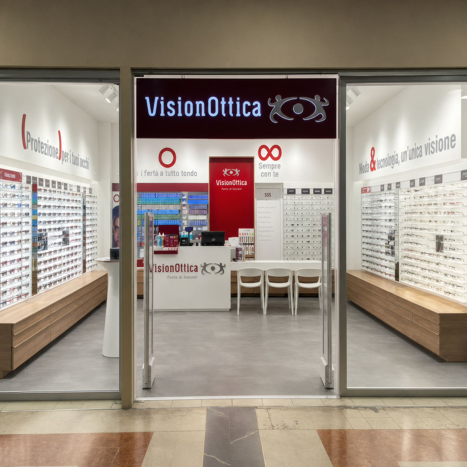 Ingresso del negozio VisionOttica Porte di Sassari di Sassari in centro commerciale con insegna scura con logo e testo, apertura centrale con porta a vetri su interno con espositori a parete di montature e bancone interno visibile