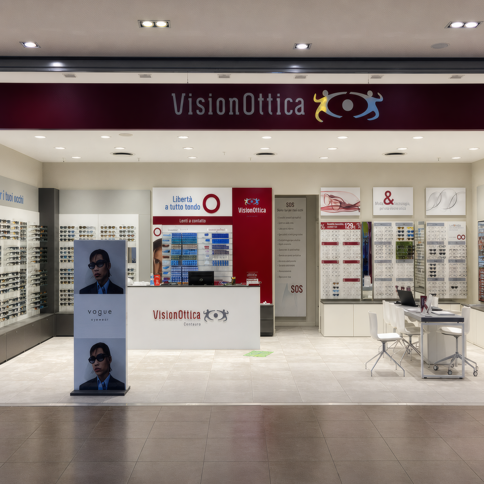 Ingresso del negozio VisionOttica Centauro di Chieti in centro commerciale con insegna bordeaux, apertura ad arco su interno con bancone bordeaux centrale, scaffali laterali di occhiali e totem promozionale con immagine di modello
