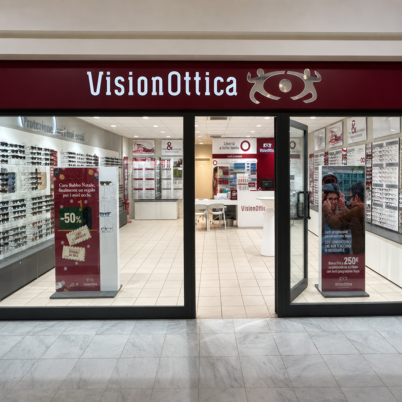 Ingresso del negozio VisionOttica Leudi di Genova in centro commerciale con insegna bordeaux, ampia vetrata aperta e espositori di occhiali sui lati