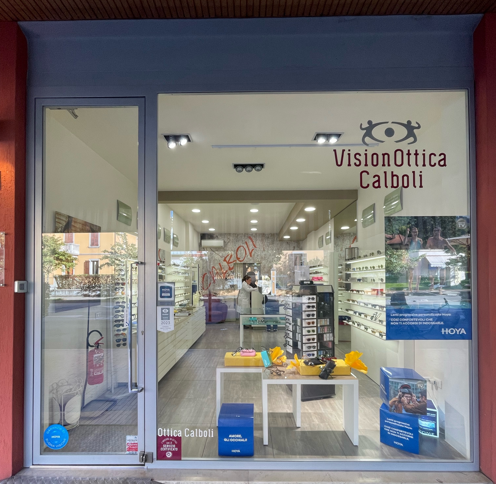 Vetrina del negozio VisionOttica Calboli di Forlì su strada con insegna bordeaux, ampia superficie a vetro che mostra l'interno con espositori di montature e bancone di consultazione
