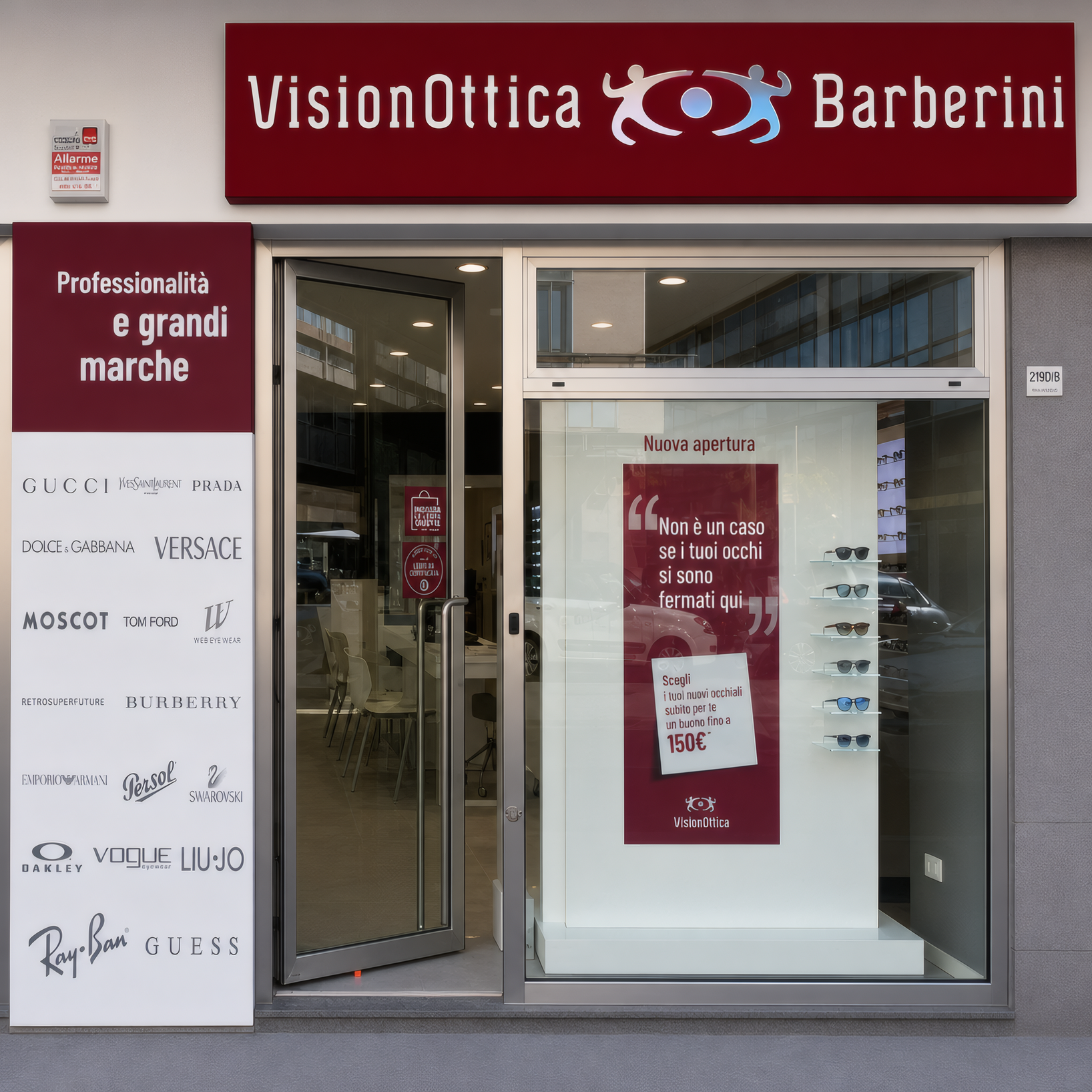 Facciata del negozio VisionOttica Barberini di Montesilvano su strada con insegna bordeaux, vetrina con pannello marchi di lusso a sinistra e vetrina con testo promozionale a destra