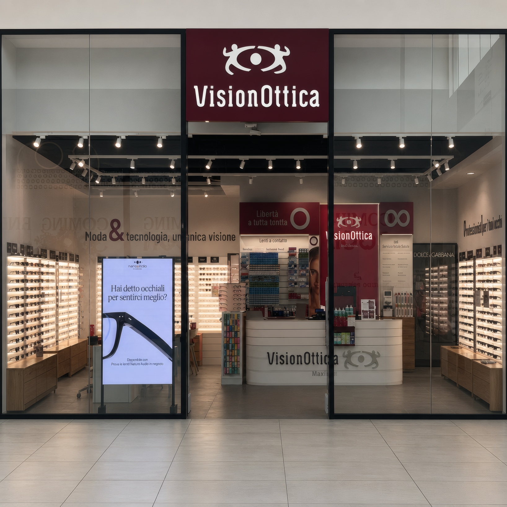 Ingresso del negozio VisionOttica Maximall di Torre Annunziata in centro commerciale con insegna bordeaux, vetrata aperta e interno con scaffali di montature e totem promozionale digitale