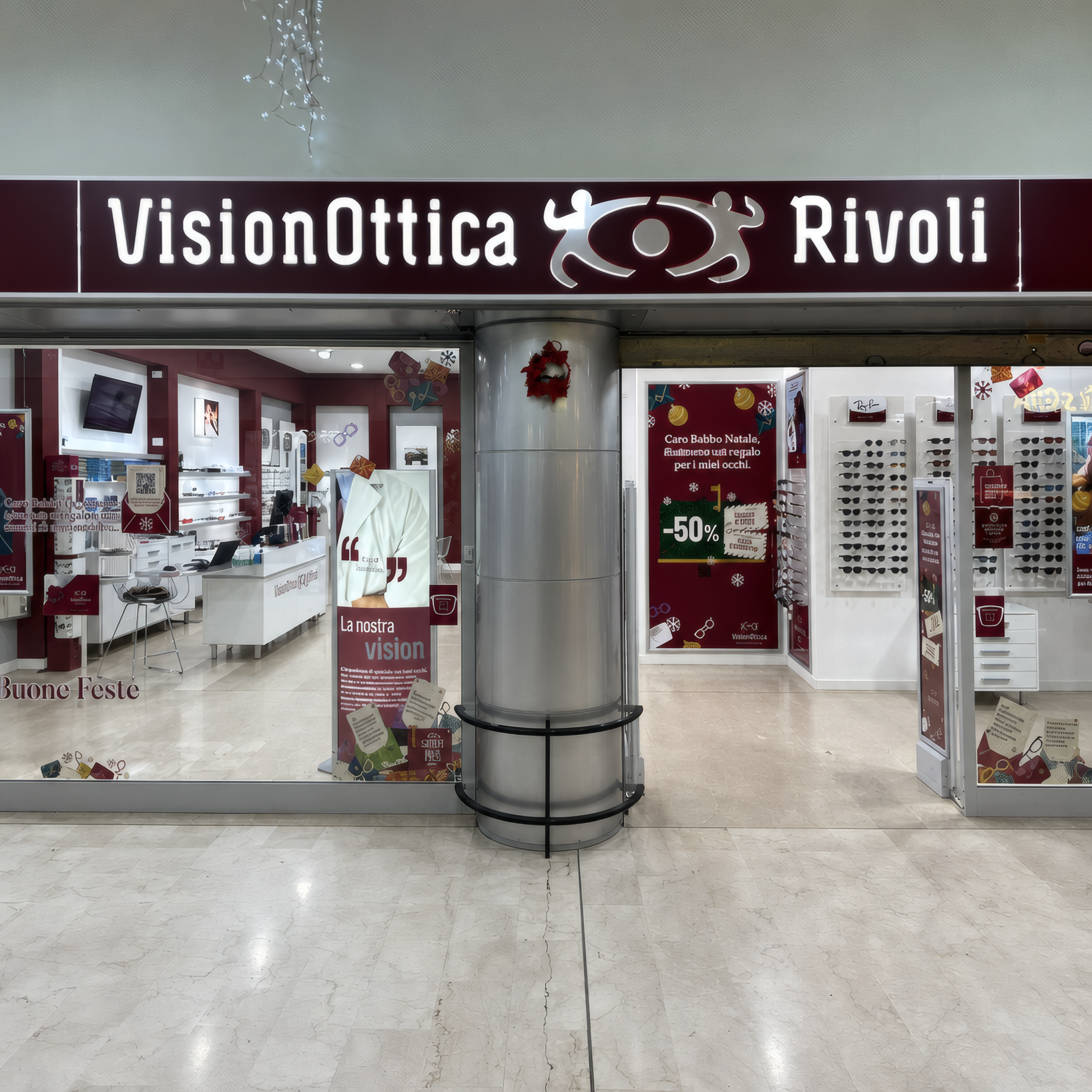Ingresso del negozio VisionOttica Rivoli di Rivoli in centro commerciale con insegna bordeaux con nome del negozio, vetrata frontale e interno con espositori di occhiali e banner promozionali