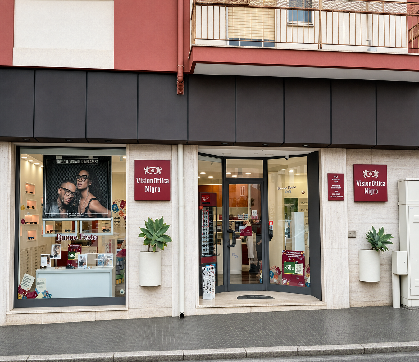 Ingresso del negozio VisionOttica Nigro di Brindisi su strada con porta a vetri scura, insegna bordeaux e vetrina con poster di occhiali da sole