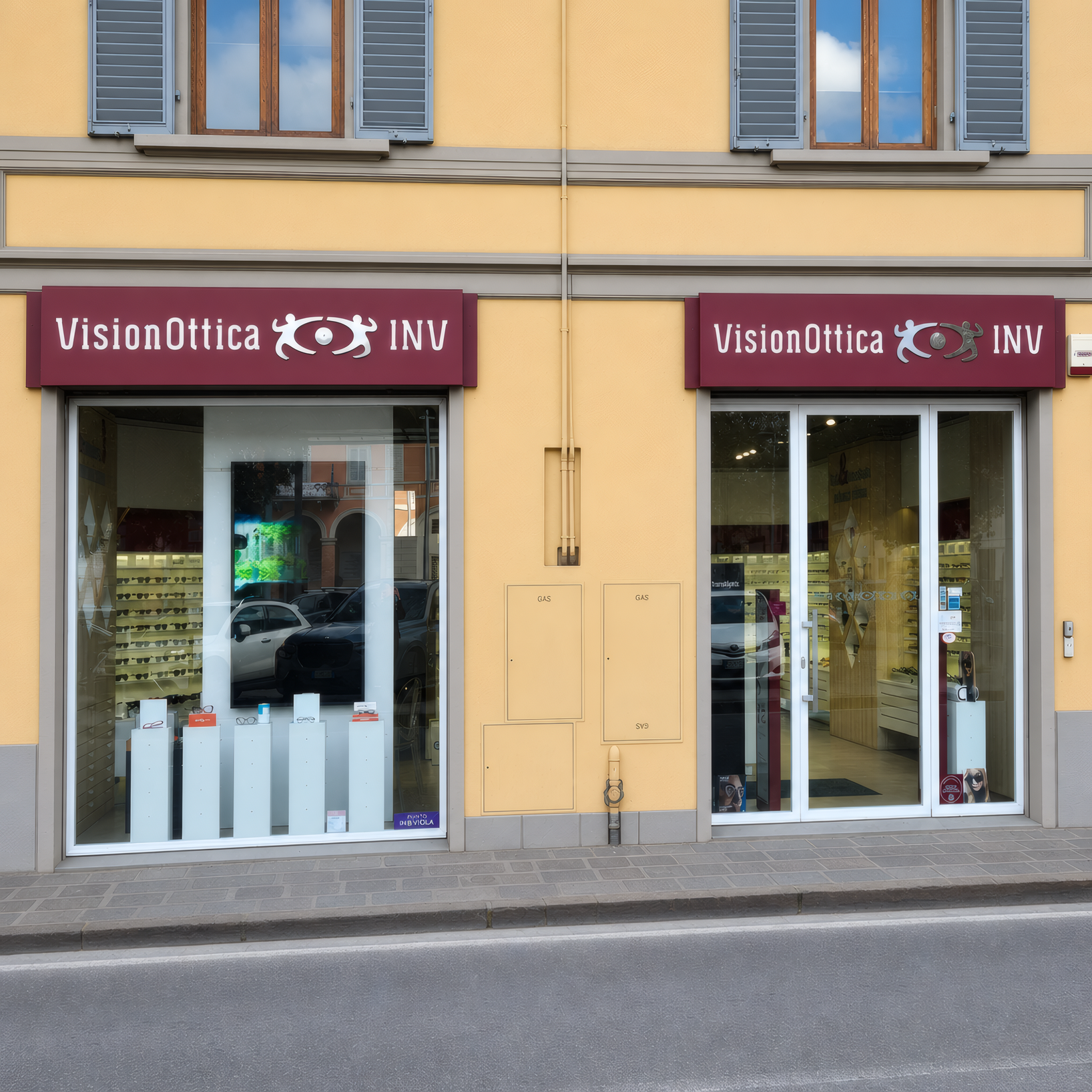 Facciata del negozio VisionOttica INV di Scandicci su strada con doppia vetrina luminosa, insegne bordeaux e edificio con intonaco giallo