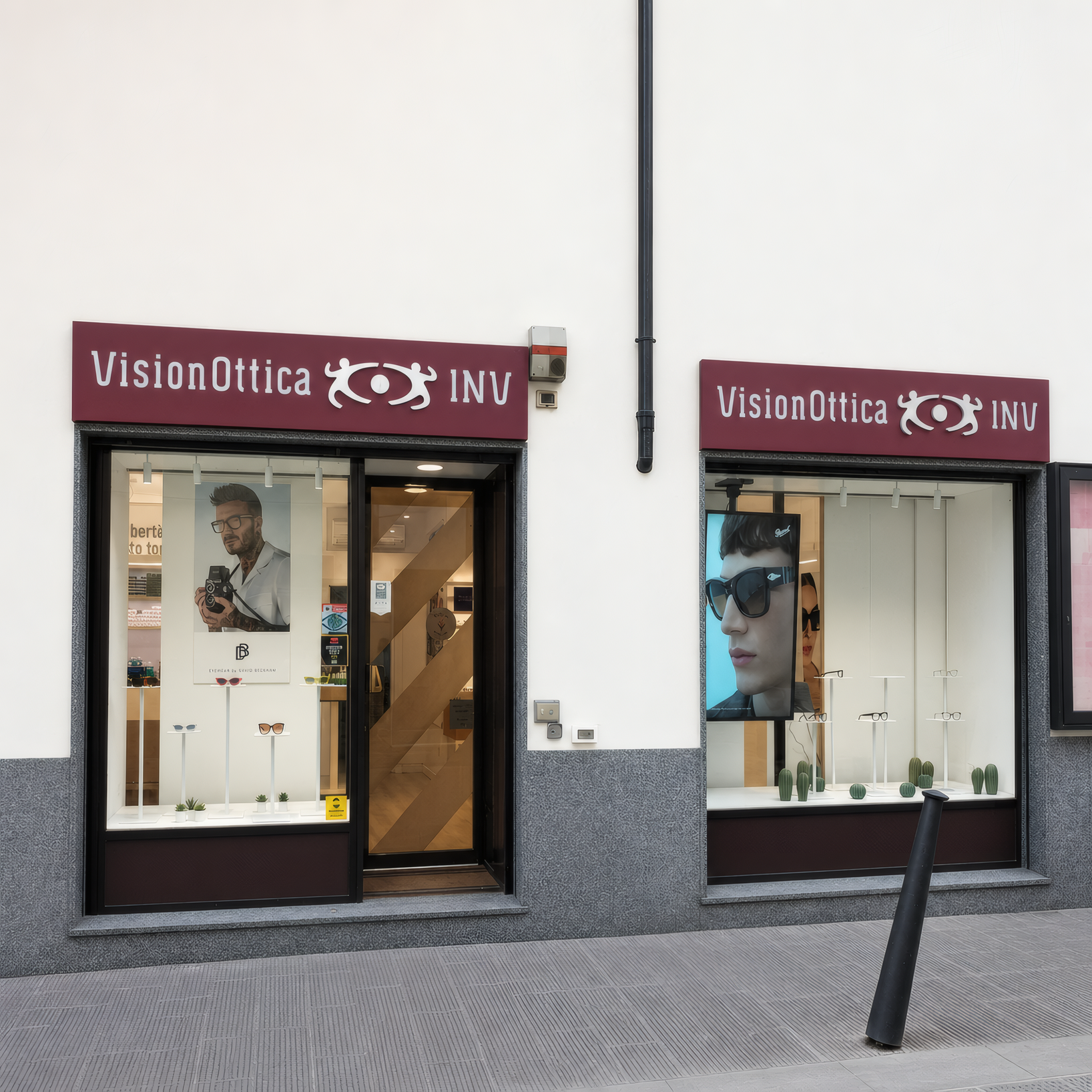 Facciata del negozio VisionOttica INV di Firenze su strada con doppia insegna bordeaux, due vetrine con poster di modelli in occhiali e porta centrale