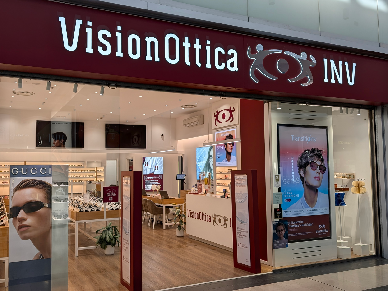 Ingresso del negozio VisionOttica INV di Sesto Fiorentino in centro commerciale con vetrina ampia, insegna bianca e schermi pubblicitari con brand Gucci