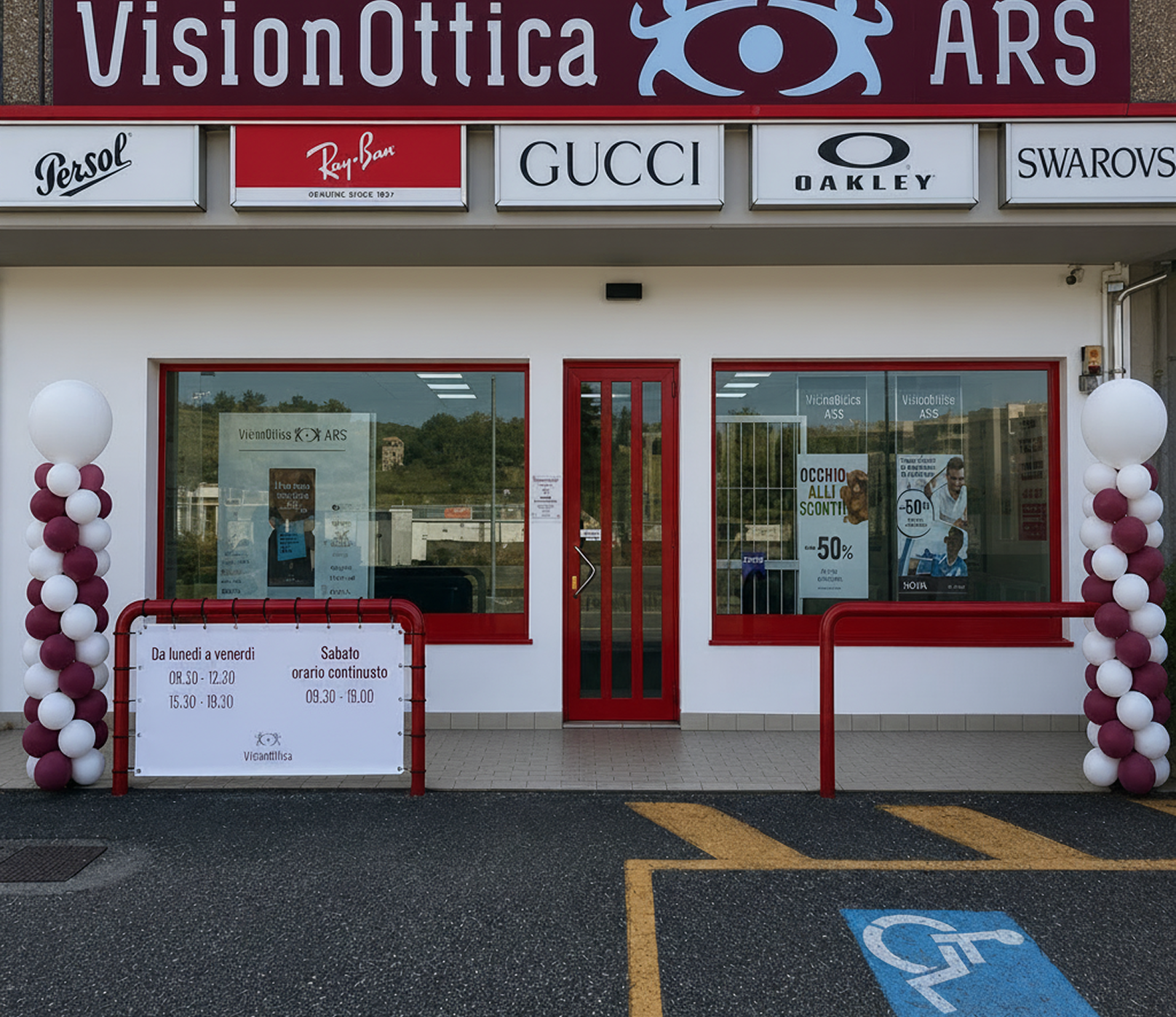 Facciata del negozio VisionOttica ARS di Mercallo su strada con insegna bordeaux e bianca, porta rossa, banner di brand Persol Gucci Oakley e palloncini decorativi