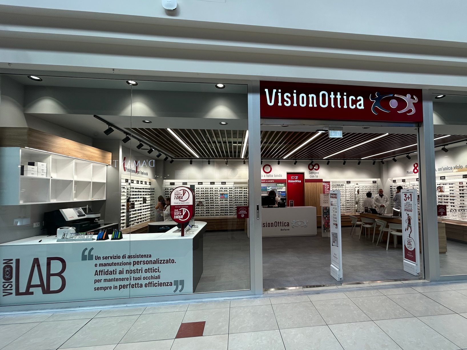 Ingresso del negozio VisionOttica Le Befane di Rimini in centro commerciale con vetrina aperta, area Vision Lab con bancone e espositori a parete