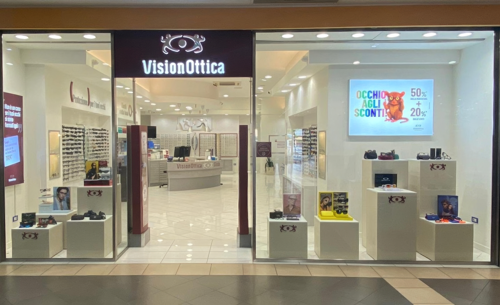 Ingresso del negozio VisionOttica Globo di Lugo in centro commerciale con vetrina e espositori di occhiali, banner digitale con promozione e insegna nera