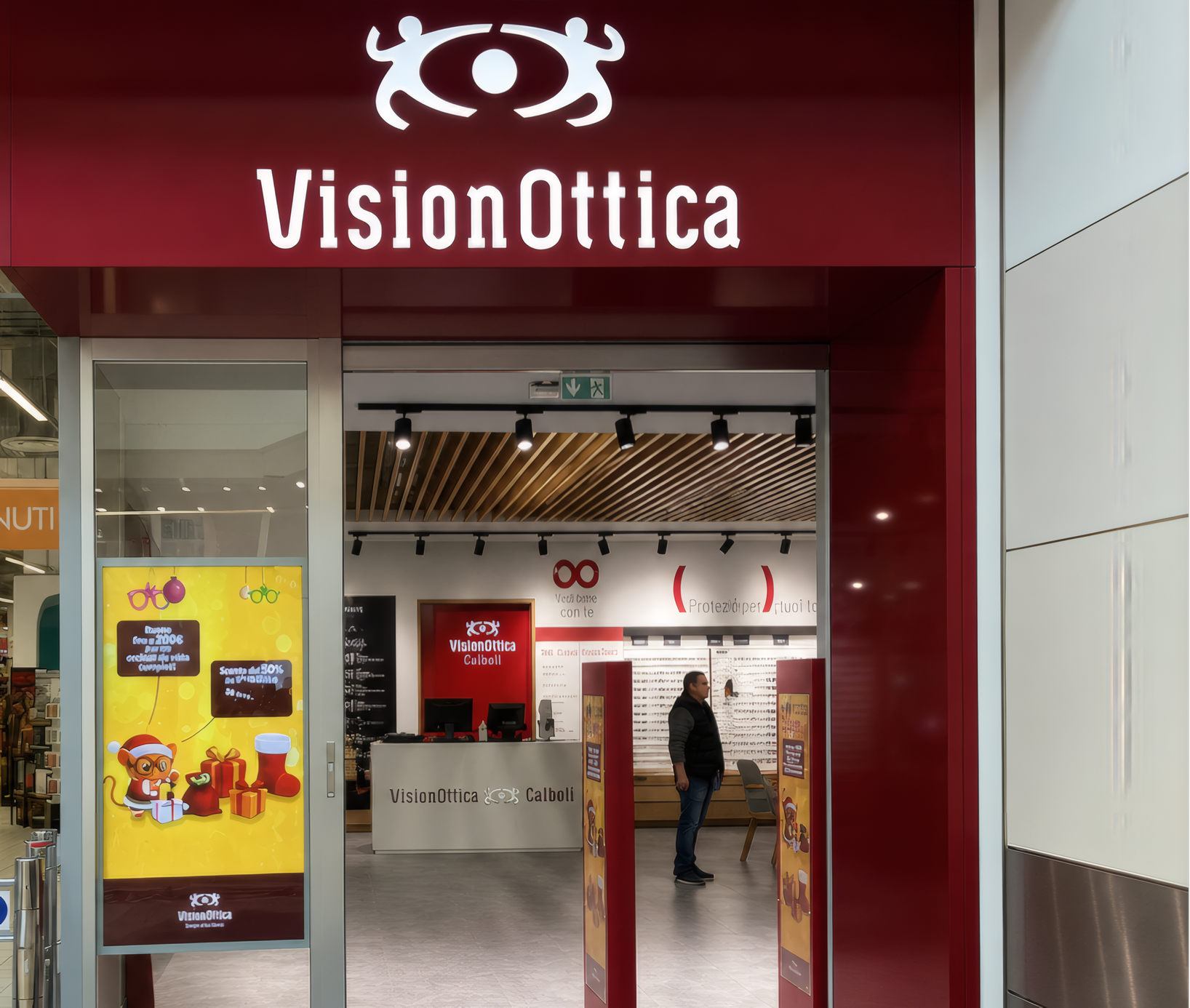 Ingresso del negozio VisionOttica Calboli di Forlì in centro commerciale con insegna bordeaux, porta a vetri aperta e banner promozionali laterali