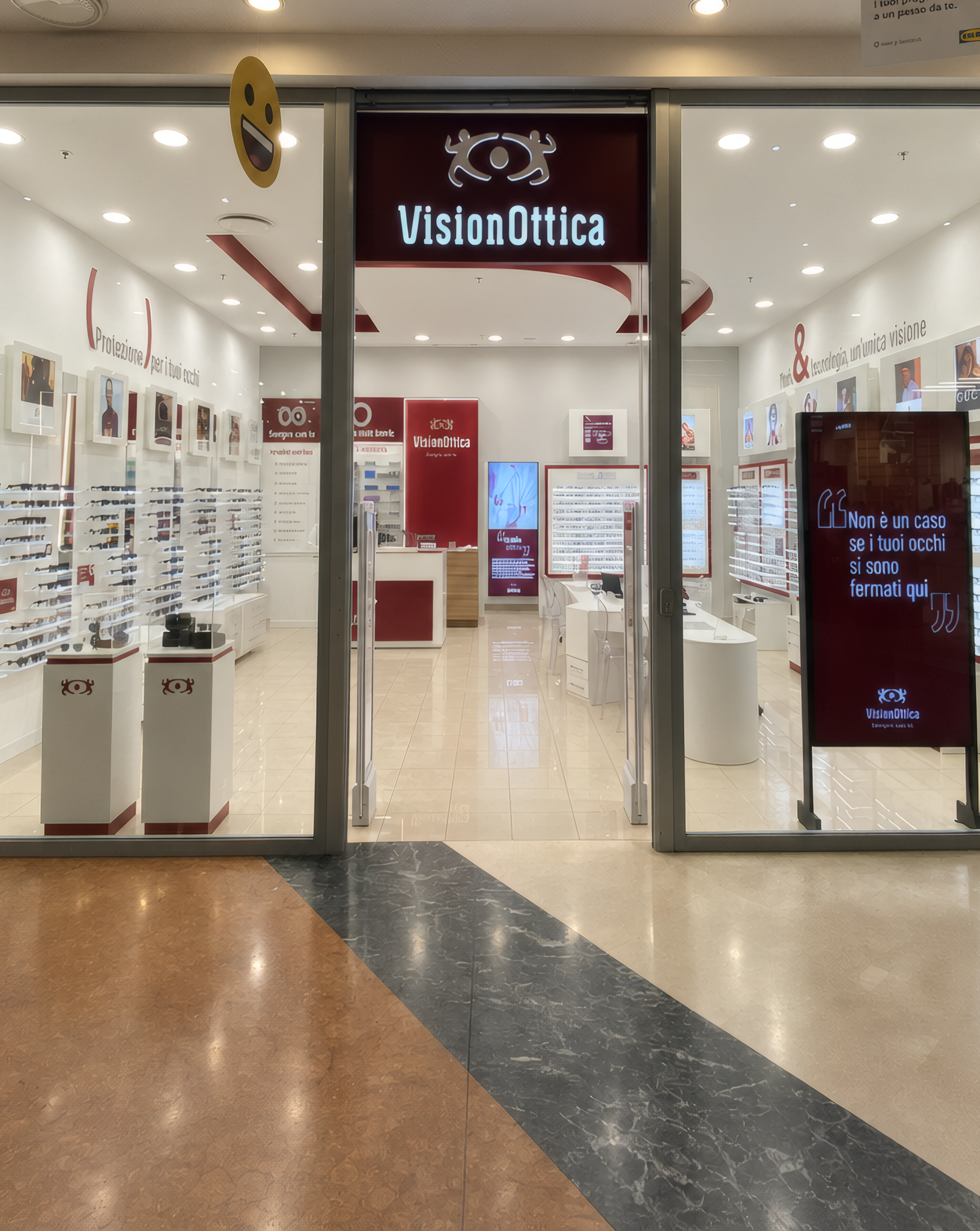 Ingresso del negozio VisionOttica Porto Bolaro di Reggio Calabria in centro commerciale con insegna bordeaux, espositori di montature ai lati e totem promozionale interno
